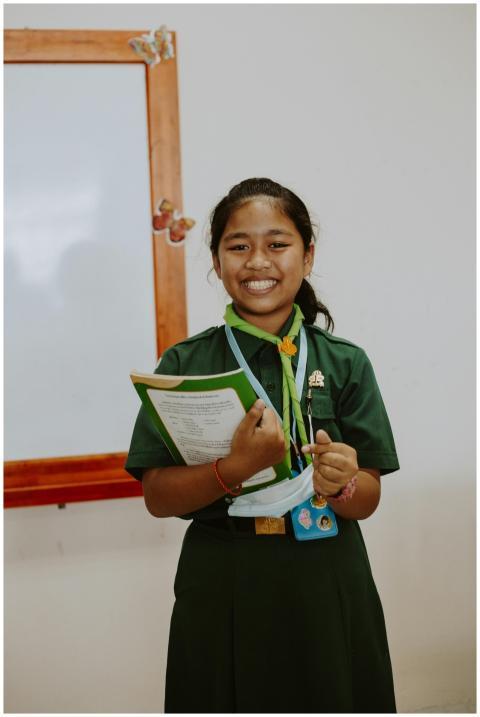 Cheerful student in uniform holding a notebook, st