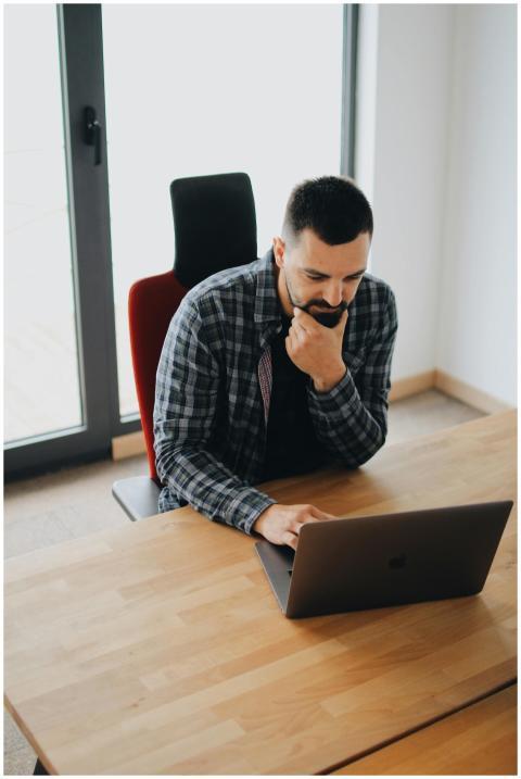 Young man with beard working on laptop at desk in