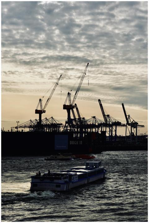 A cargo ship passes a busy industrial port with cr