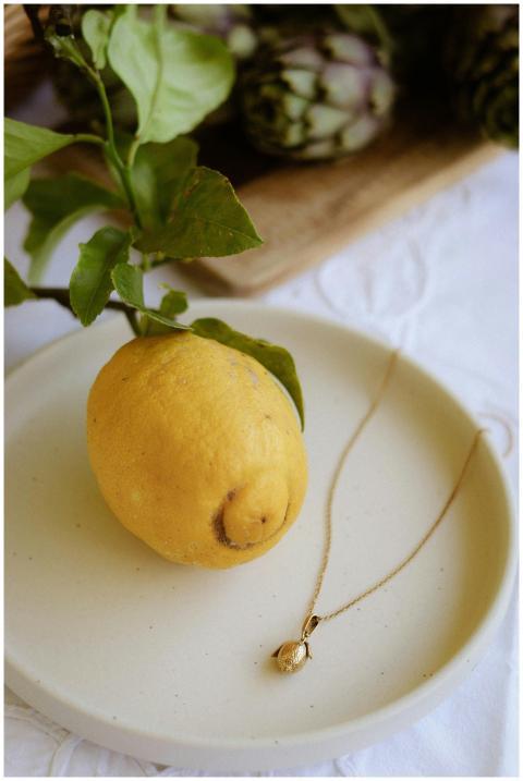 Lemon with gold necklace on plate, artichokes in s