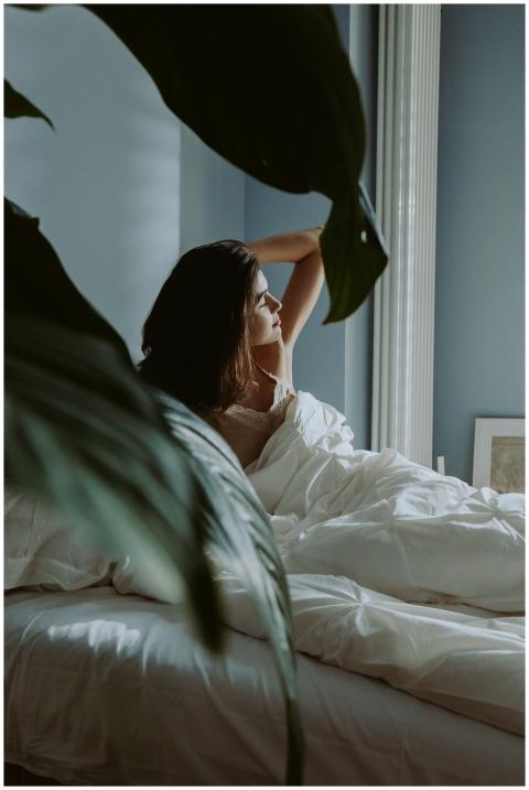 A woman waking up in a sunlit bedroom, surrounded