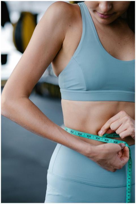 Female athlete measuring waistline with tape for h