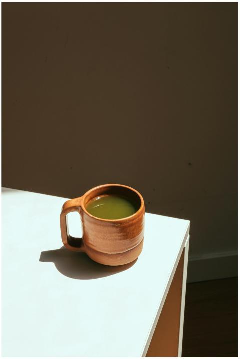 Ceramic mug with matcha latte on a sunlit white ta