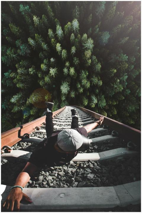 A man poses daringly over train tracks with a fore