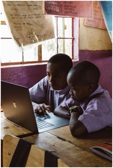 Two young boys in school uniforms focus on a lapto