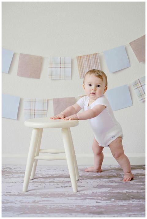 Cute baby standing by a stool indoors with a playf