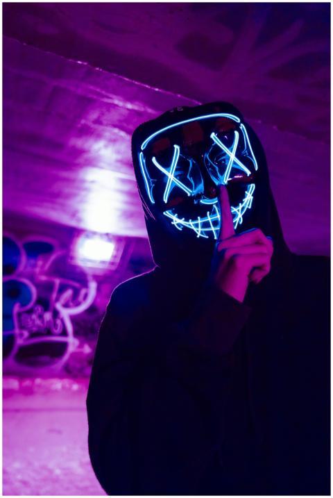 Eerie figure wearing a neon LED mask in a dimly li
