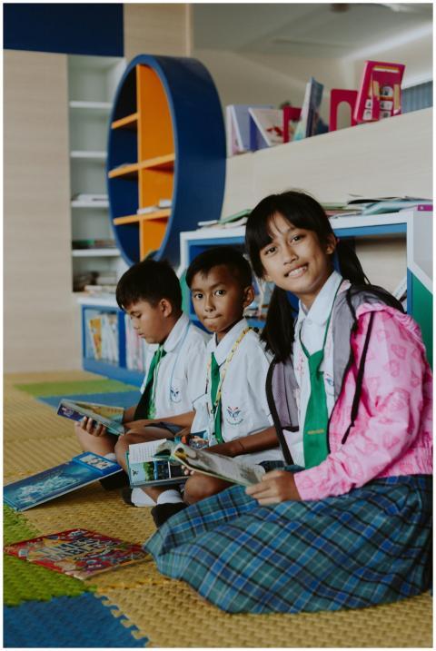 Three school children reading books in a modern li
