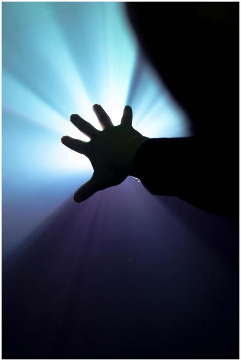 Silhouette of a hand reaching towards bright beams