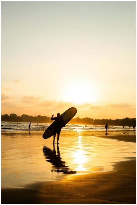 A silhouette of a surfer carrying a board at sunse