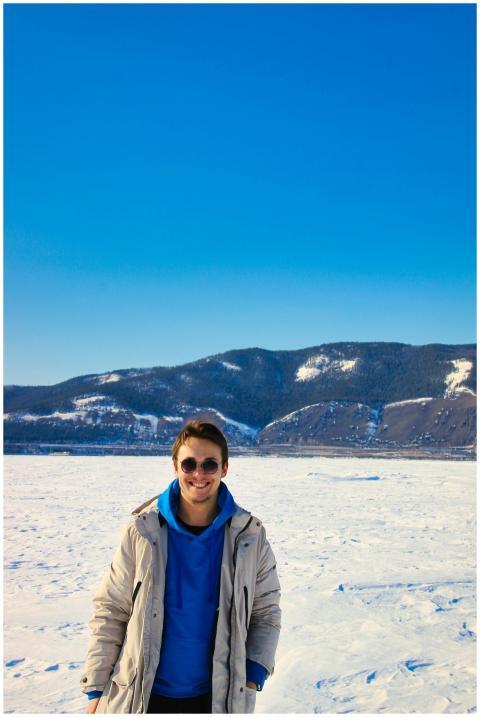 A man in a winter coat stands smiling against a st