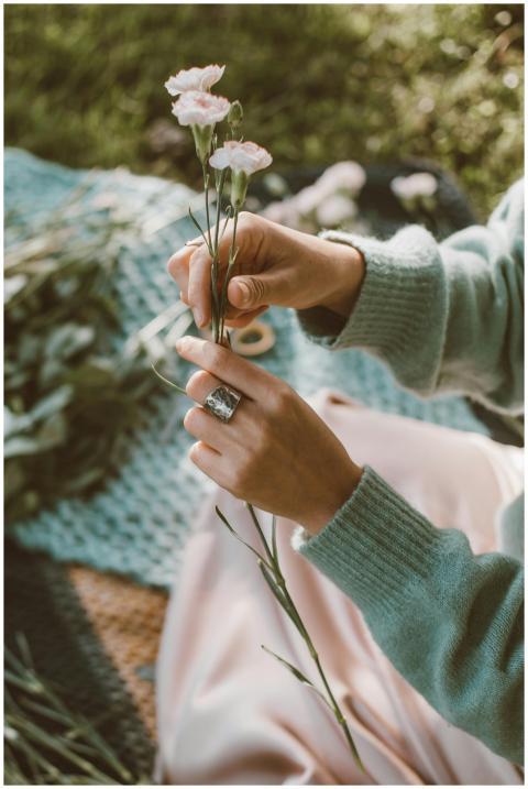 A person in a sweater holds delicate flowers, crea