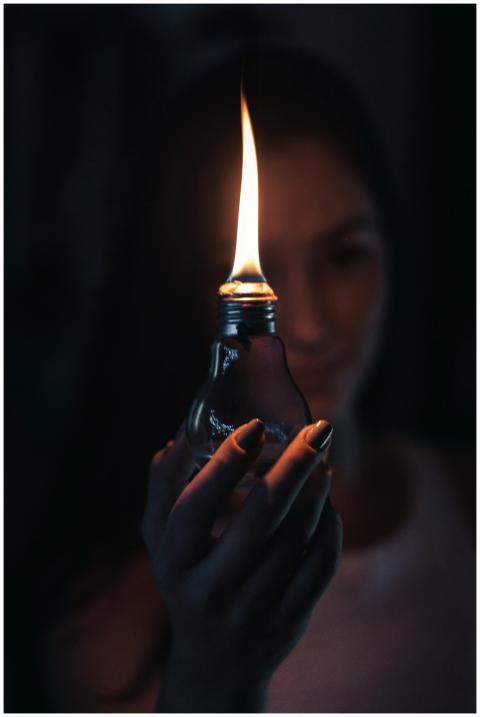 A glowing flame inside a light bulb held by a woma