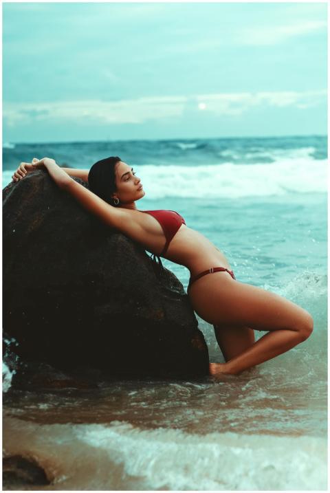 Woman posing in a red bikini on a rocky shore with