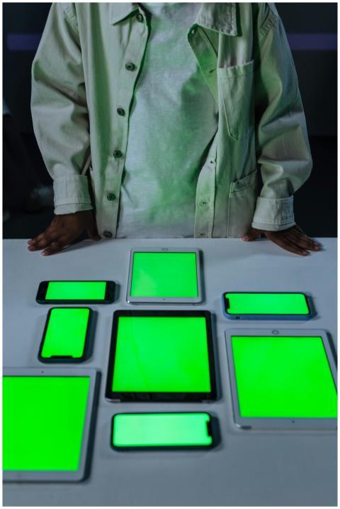 Nine digital devices on a table with green screens