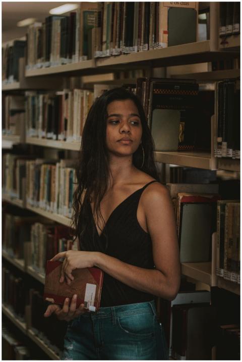 A woman stands in a library aisle, holding books a