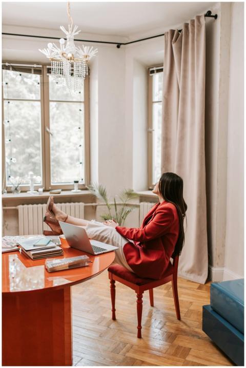 Woman in red blazer relaxing at a desk with a lapt