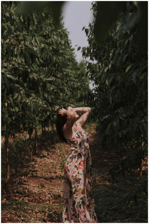 A woman in a floral sundress stands in a lush orch