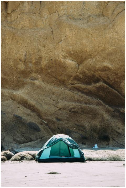 A green camping tent set against a towering rocky