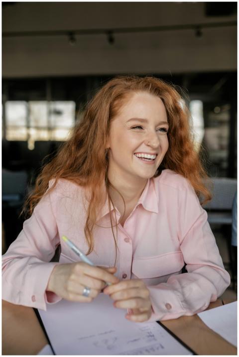 Joyful red-haired woman laughing while working in