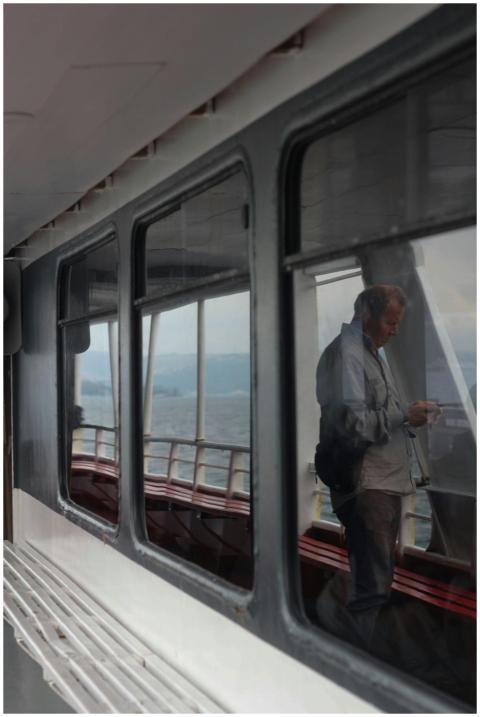 A man reflects in a window on a ferry with a sea v