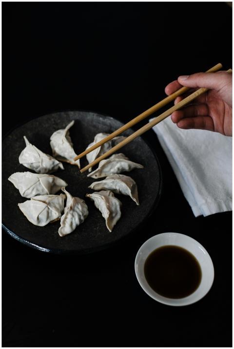 A hand using chopsticks to pick up a gyoza dumplin