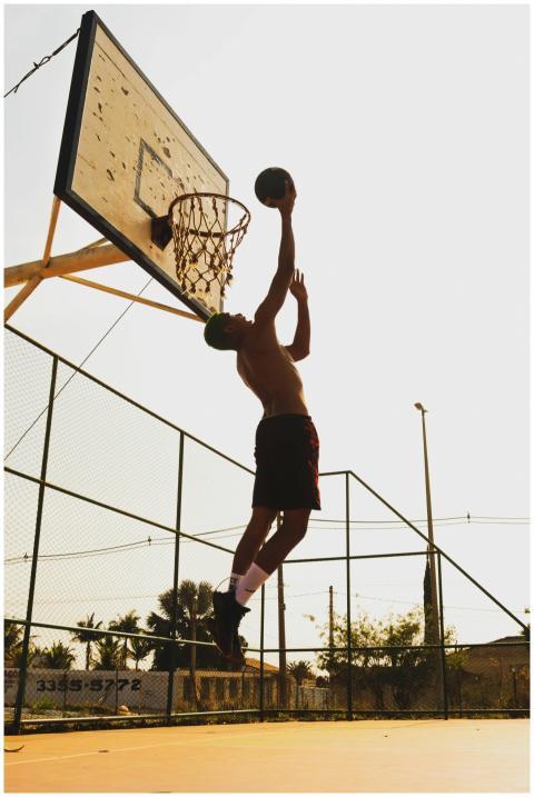 Shirtless athlete dunking basketball on outdoor co