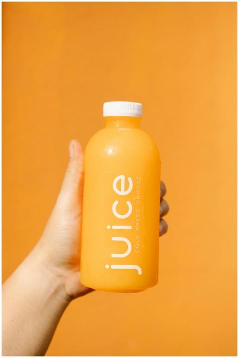 Bright orange juice bottle in hand against an oran