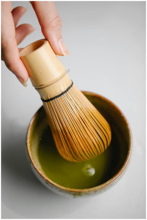 Close-up of bamboo whisk stirring matcha tea in a