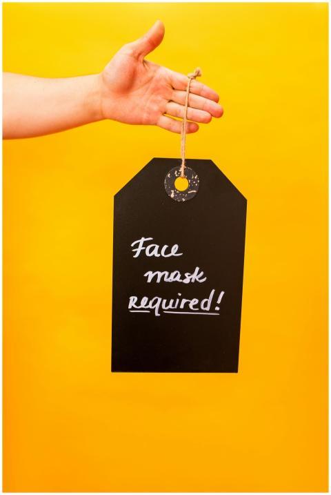 Hand holds a face mask required sign on a vibrant