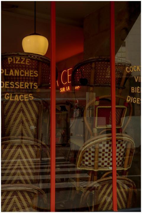 Chairs stacked in a Parisian cafe window, reflecti