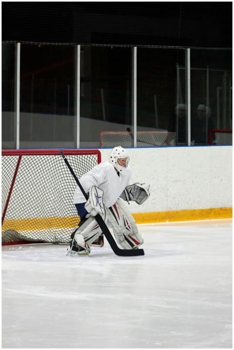 A hockey goalie in white gear stands ready to defe