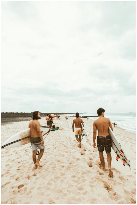 Three surfers carry their boards along a sunny bea