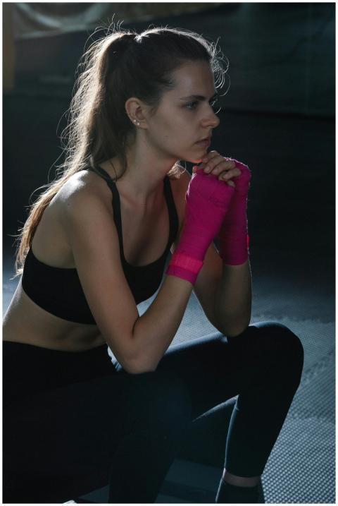 Woman in a sports bra with pink hand wraps sitting