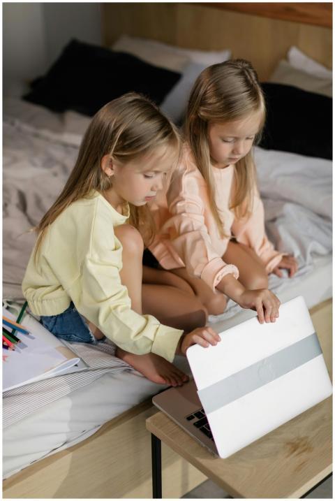 Two young girls sitting on a bed, focused on onlin