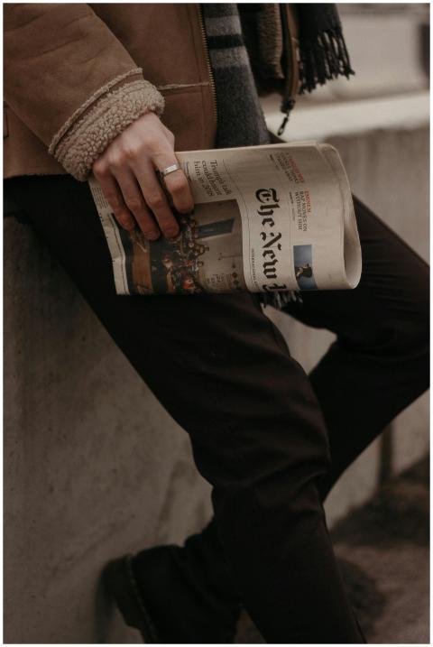 A fashionable man holds a newspaper while leaning