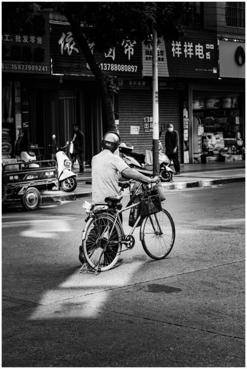 Monochrome image of a man pushing a bicycle throug