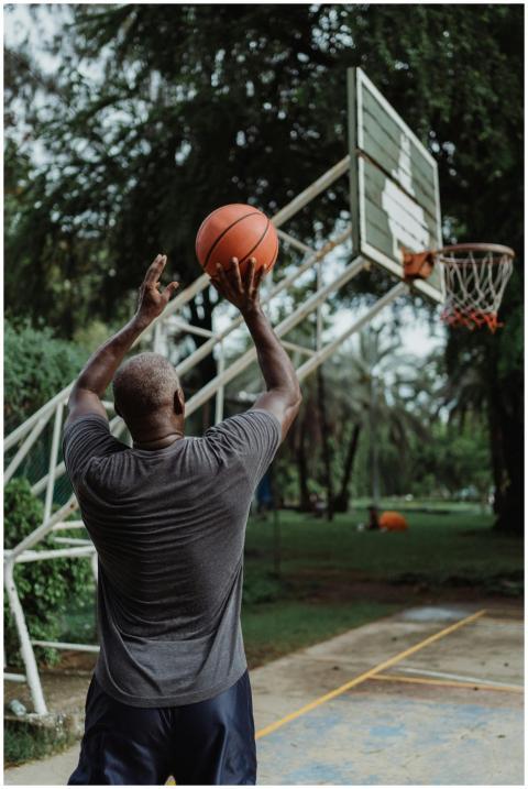 Man playing basketball in a park, aiming a shot to