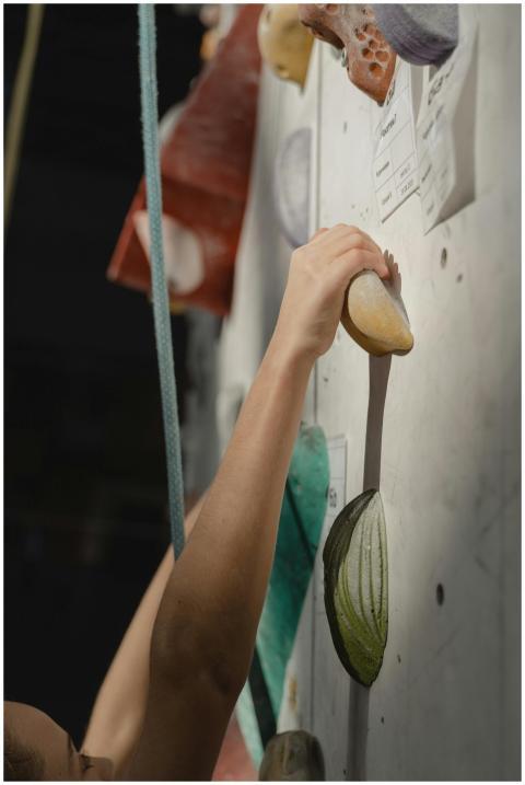 A climber's hand firmly grips an indoor climbing w