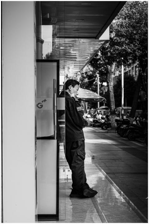 Monochrome image of a man standing on a sidewalk,
