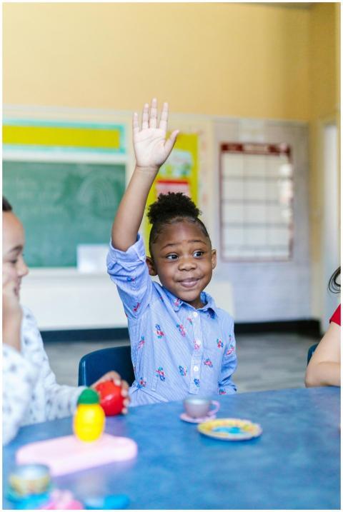 A young girl actively participates in a classroom,