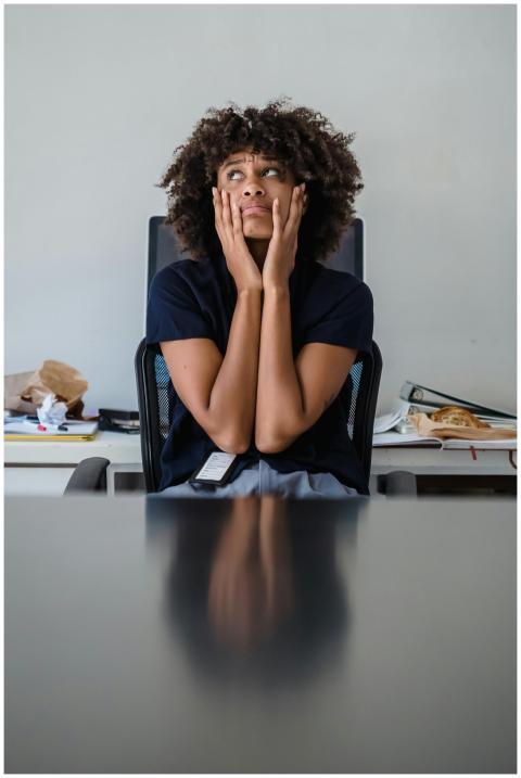Contemplative woman in office, hands on face, expr