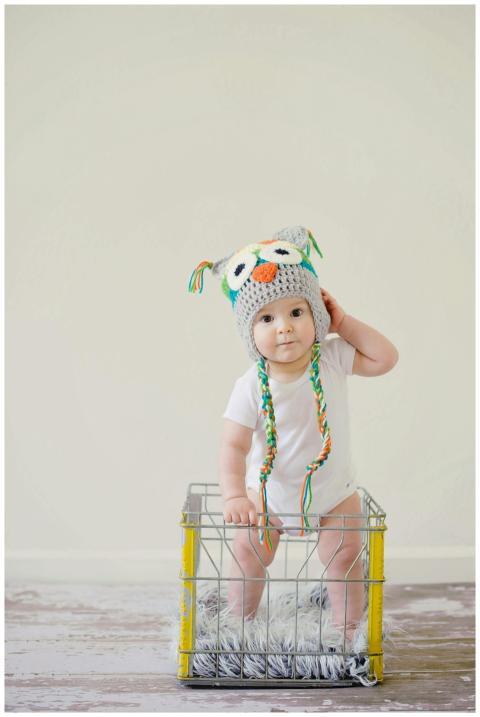 A cute baby wearing an owl hat standing in a baske