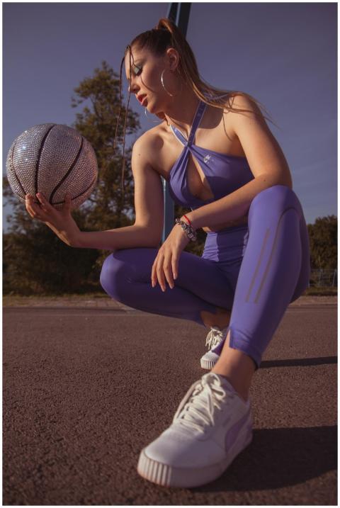 A young woman kneels on a basketball court holding