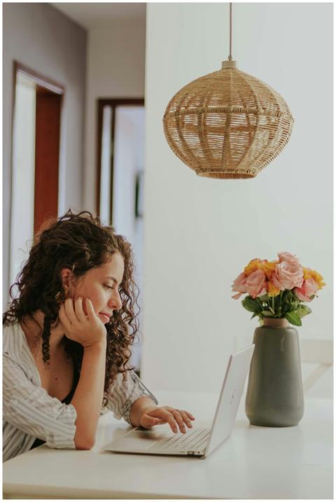 A woman uses a laptop at home with flowers and a w