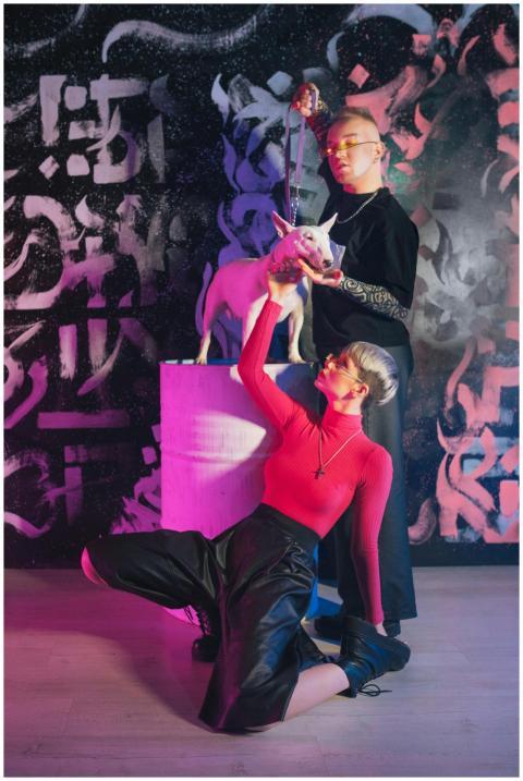 Two fashion-forward models with a dog against an a