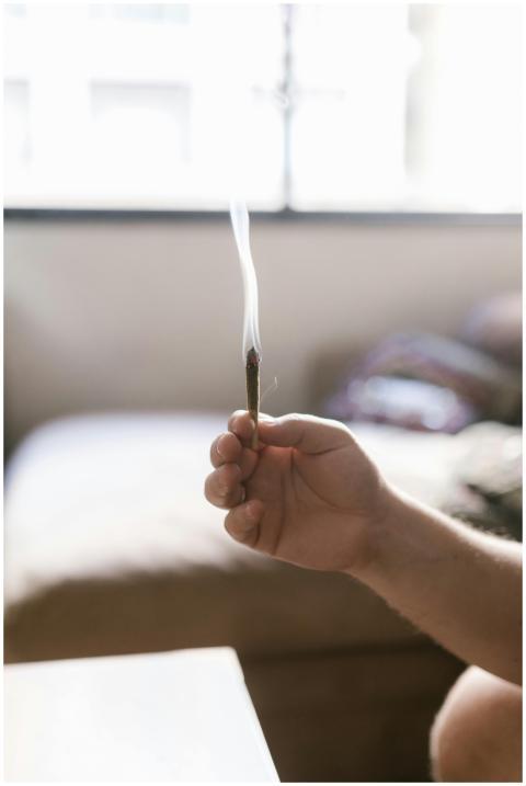 A person holding a smoking marijuana joint inside