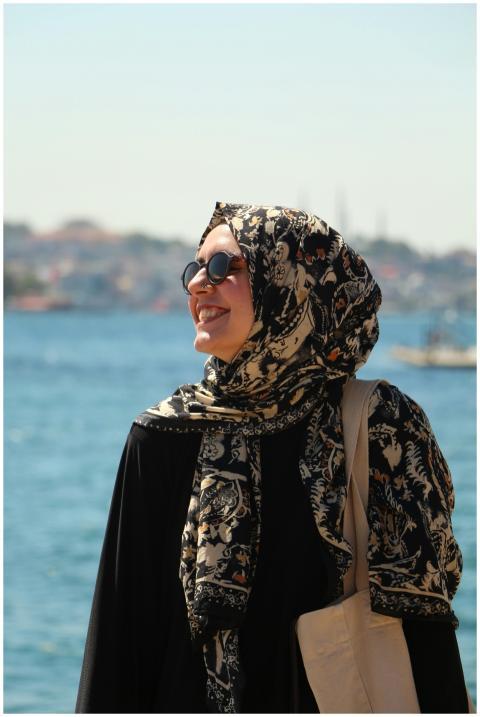 A smiling woman in hijab enjoying a sunny day by t
