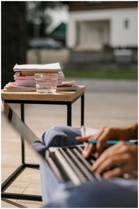 Close-up of hands typing on a laptop, glass of wat