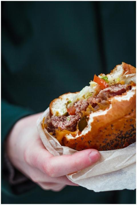 Close-up of a juicy cheeseburger held in hand, per